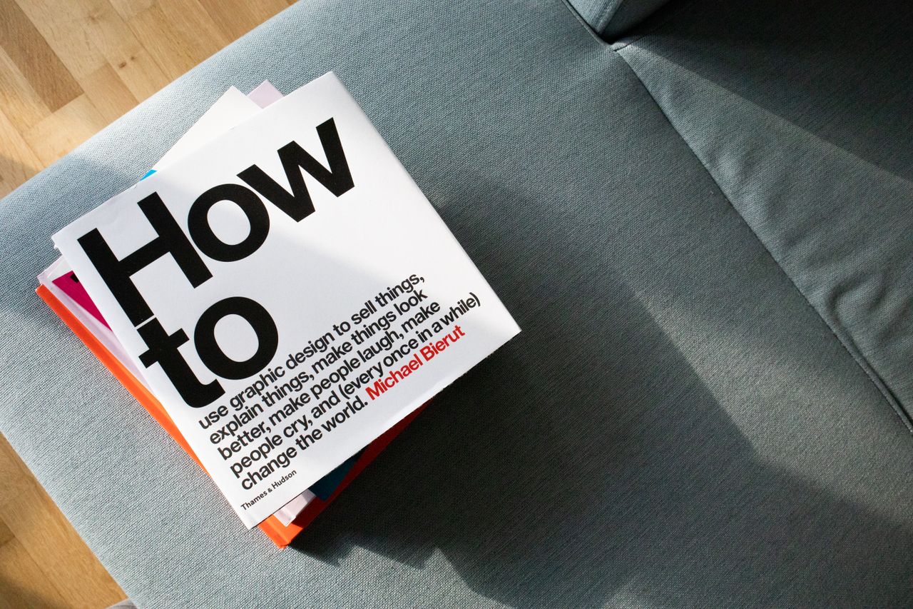 services-04 A collection of design books on a couch, showcasing How to by Michael Bierut